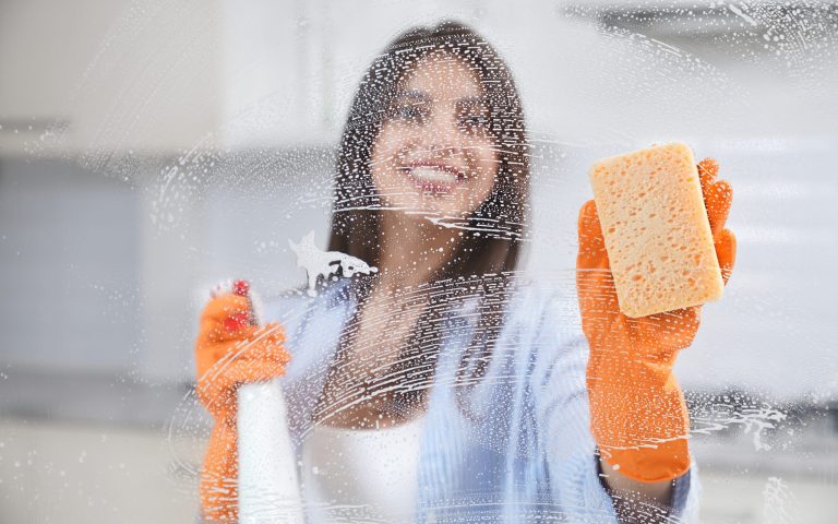 Young woman washing window in rubber gloves with special detergent. Concept of cleaning glass or window at home.