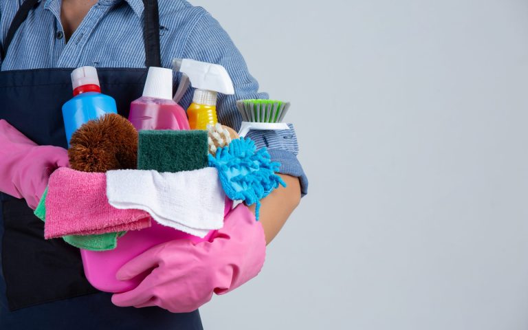 Young girl is holding cleaning product, gloves and rags in the basin on white background